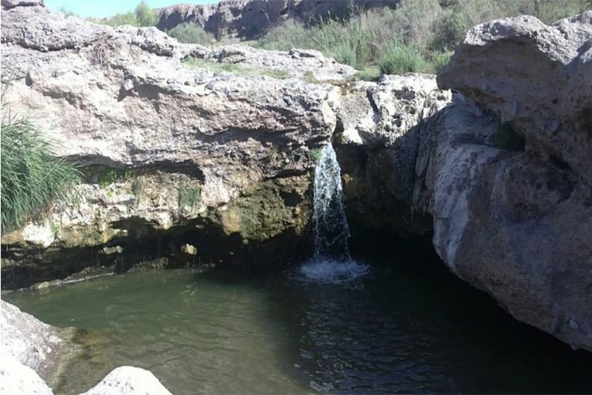 Hajin water leaving the ledge in a narrow jet under a weathered limestone overhang and falling into a still green pool