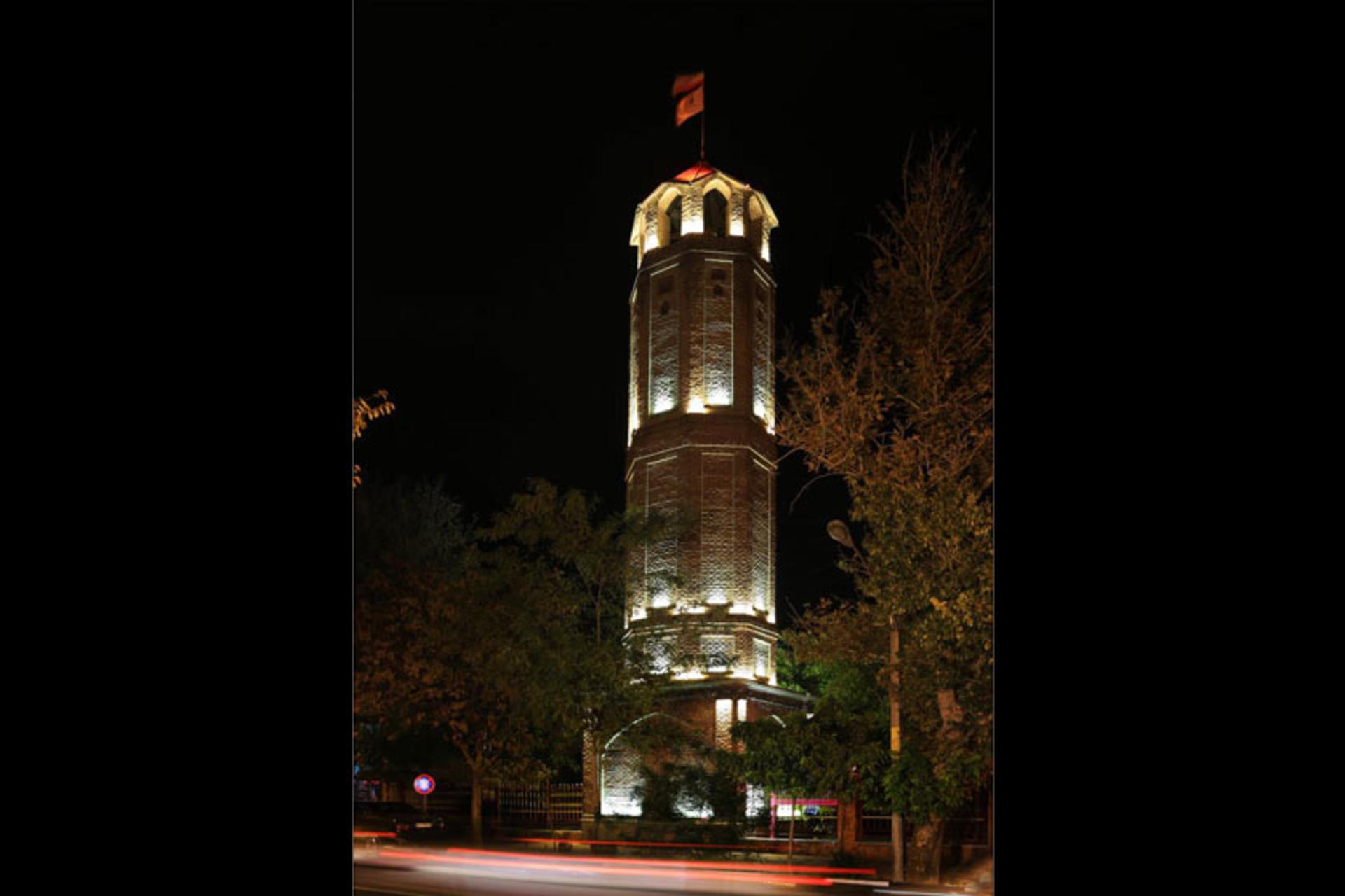 Atshanshani Tower floodlit at night, a flag on its cap and traffic light trails below