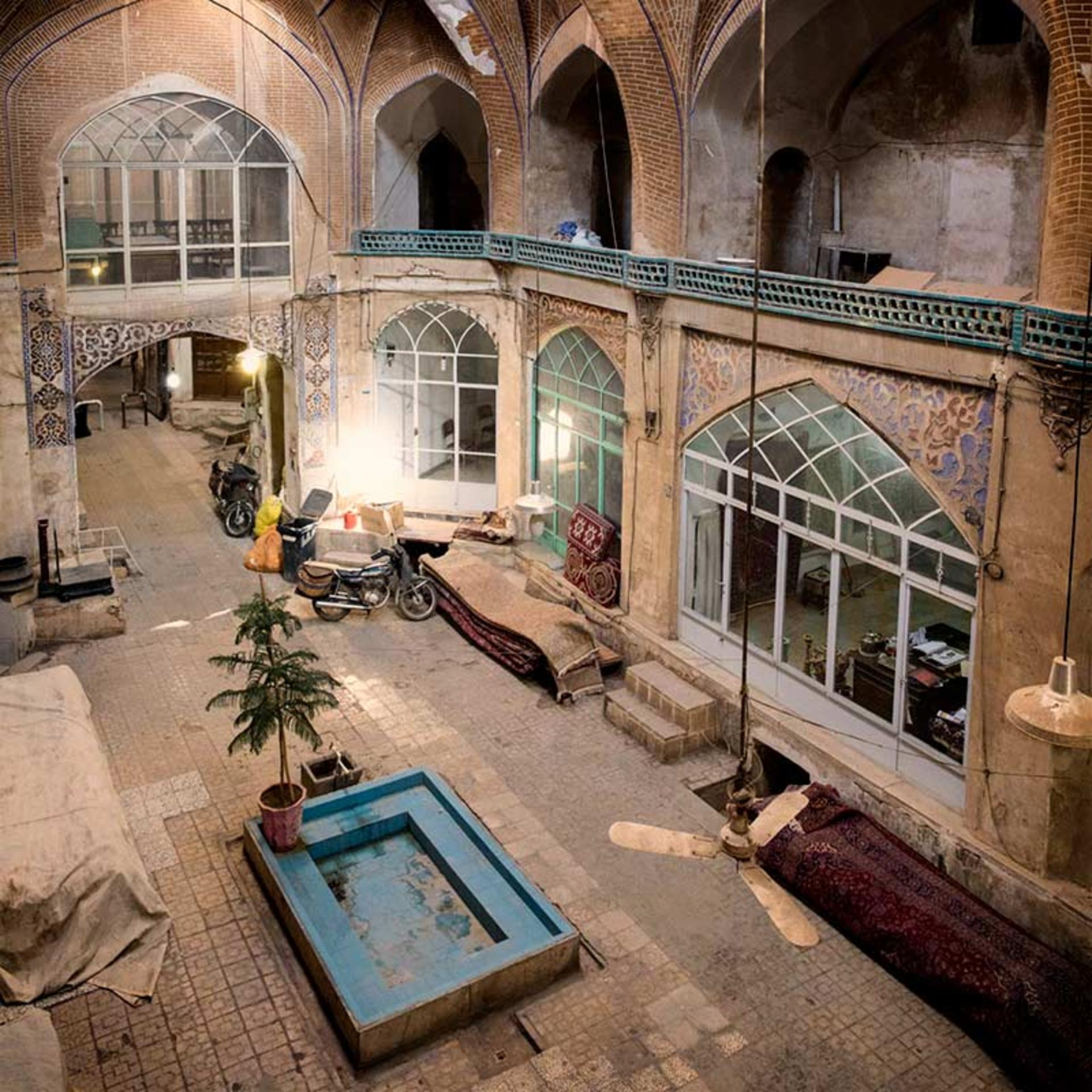 A two-storey courtyard in Kashan's old town, arched stained-glass windows above carpets and a small turquoise pool
