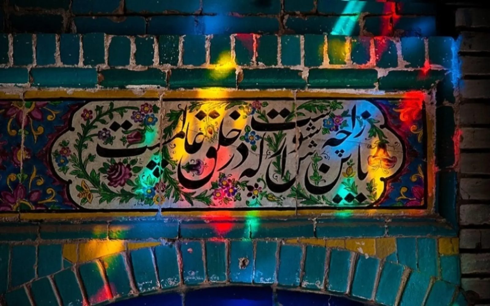 A calligraphic tile panel in Tekyeh Moaven ol-Molk lit through coloured glass