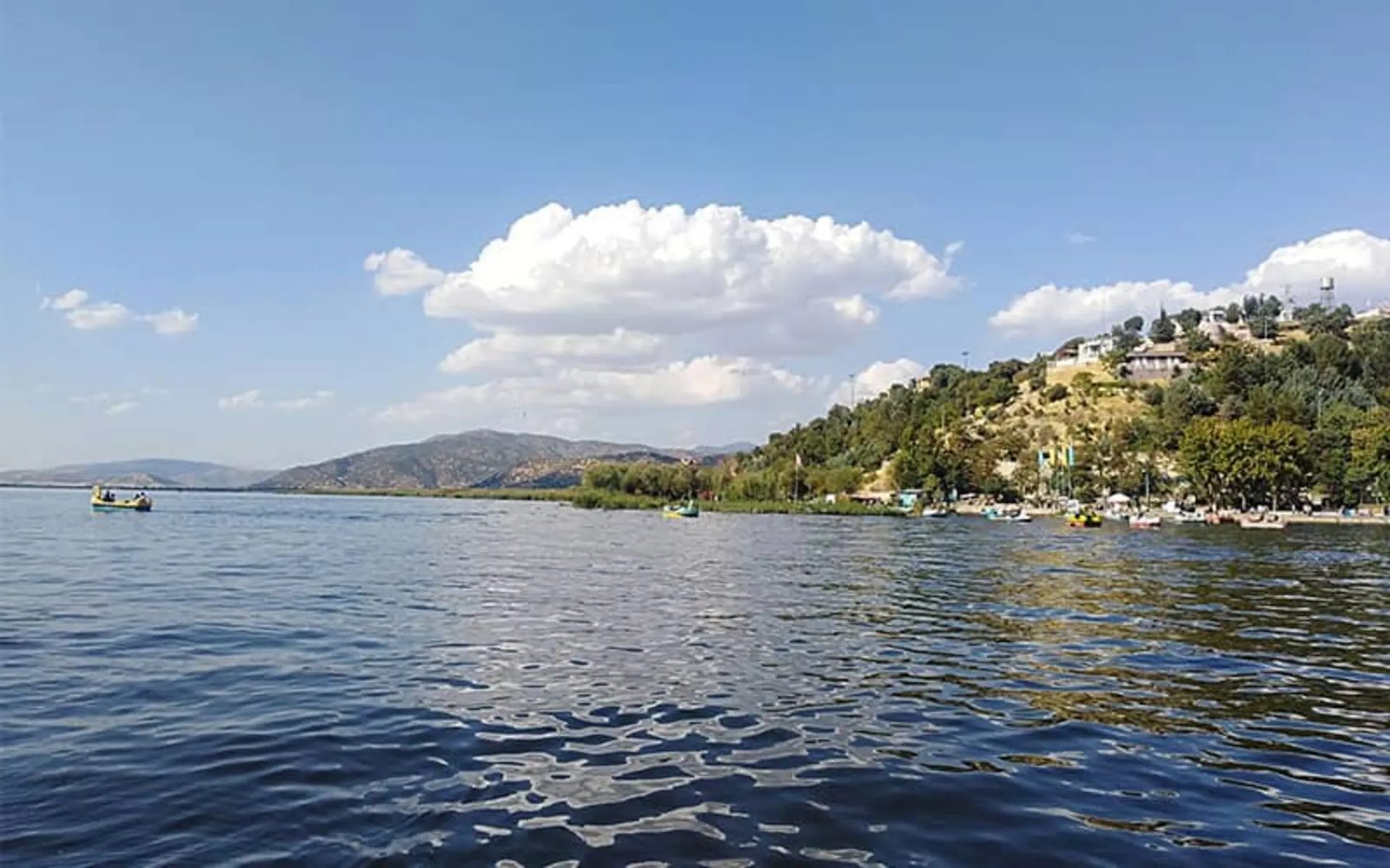 Yellow pedal boats on Lake Zarivar, a reedy shore and a wooded hill behind