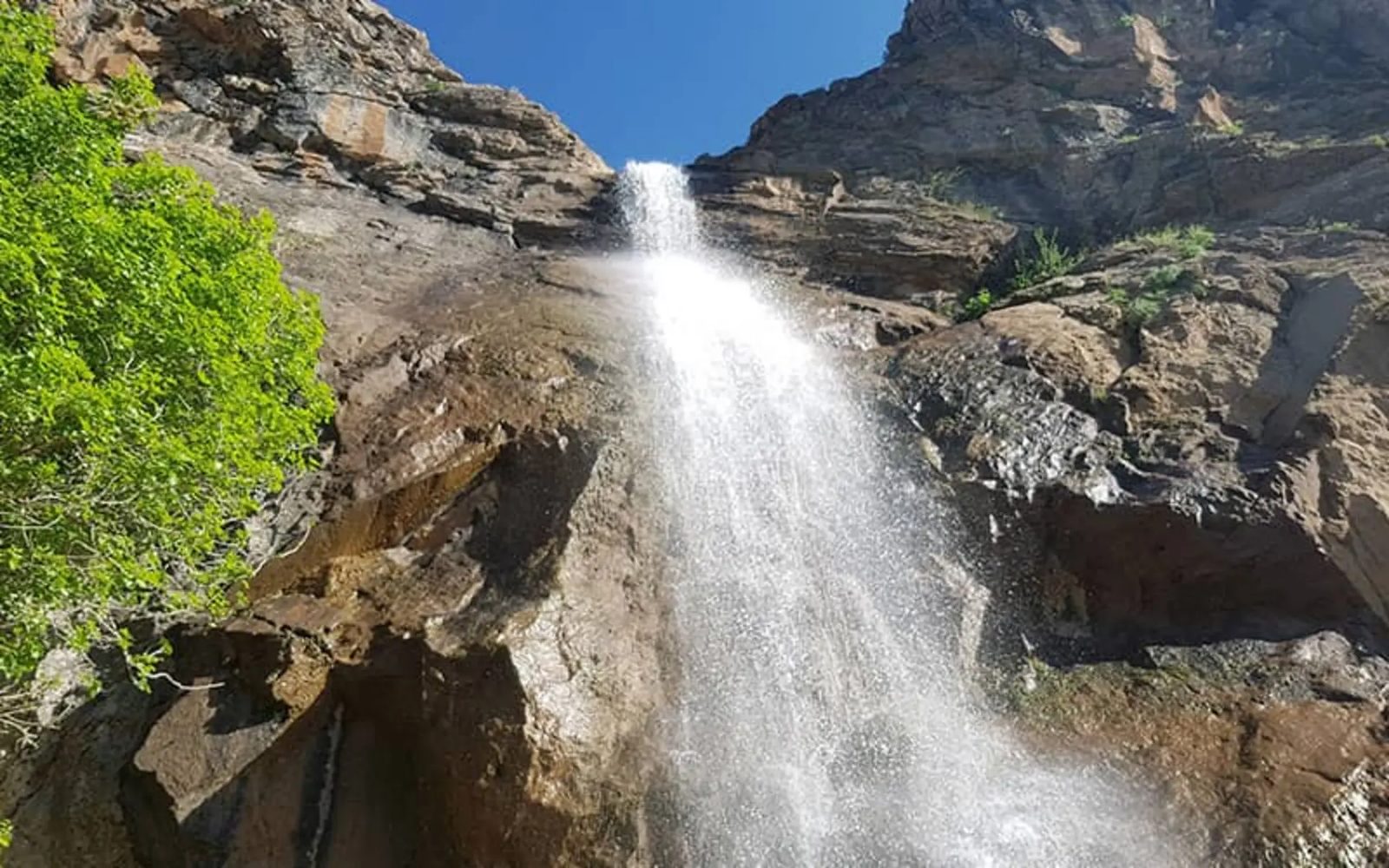 Goyleh waterfall dropping over a rock cliff, green foliage at the left and blue sky above