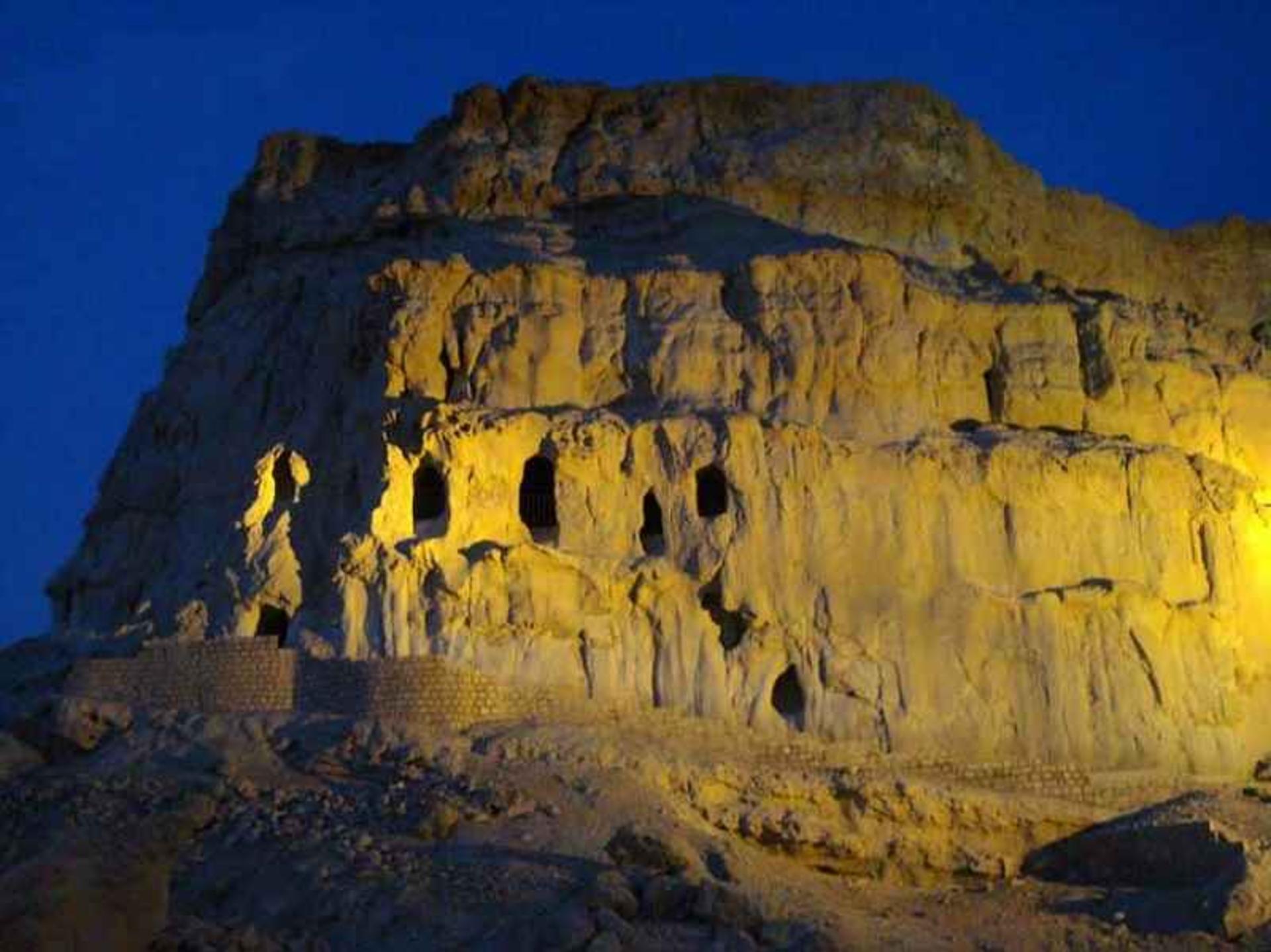 Floodlit cave openings glowing on the cliff face of Kharbs Cave at night