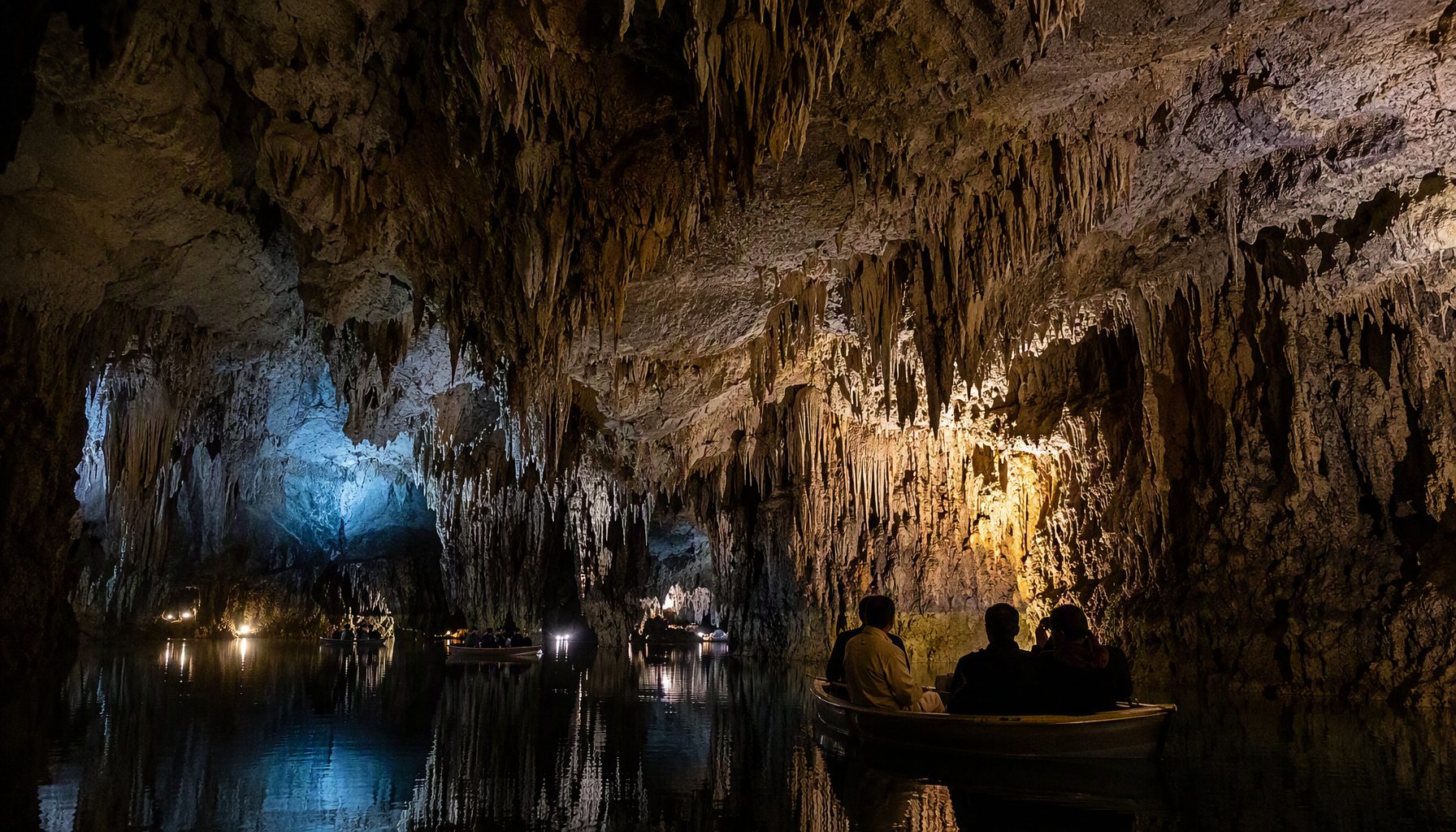 Boats gliding through the underground lake of Ali Sadr Cave with stalactites above