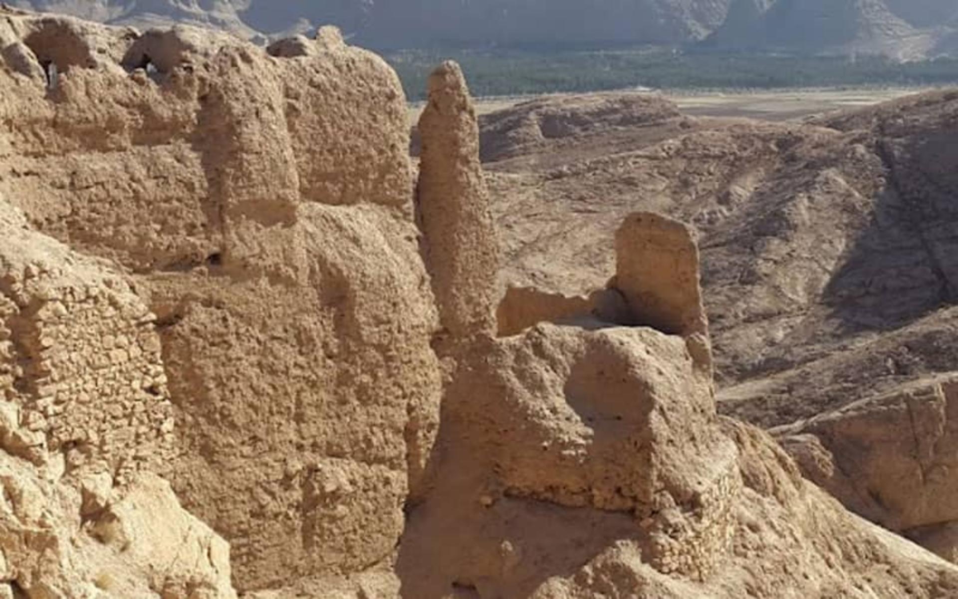 كتلٌ منهدمةٌ من الجدران على القمة، وبارٌ رفيعٌ من اللبن قائمٌ بينها، وسفوحٌ صحراوية تنحدر من خلفها