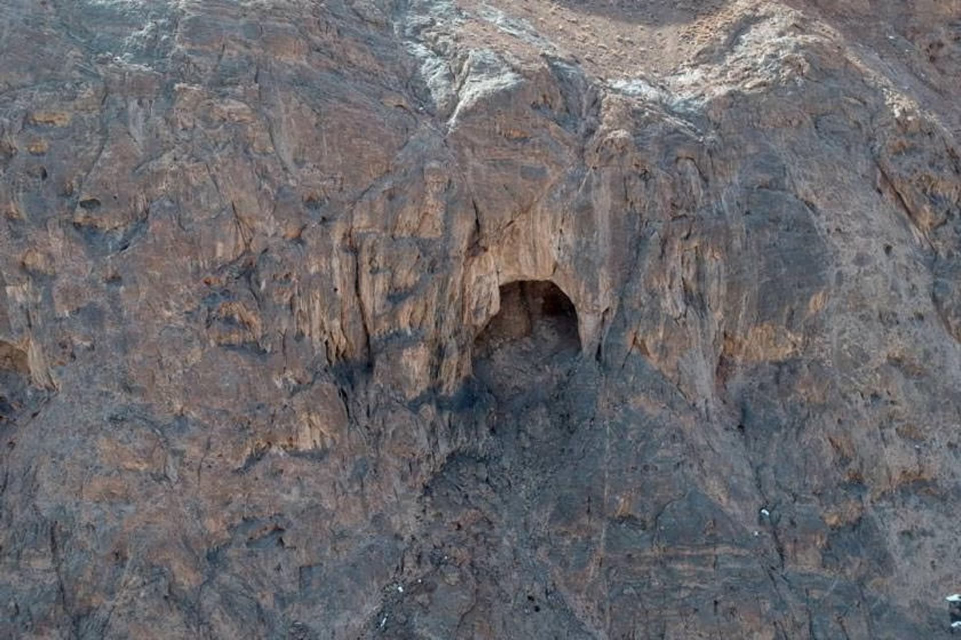 Ashkeft Cave seen from below, its arched mouth set high in a bare rock face
