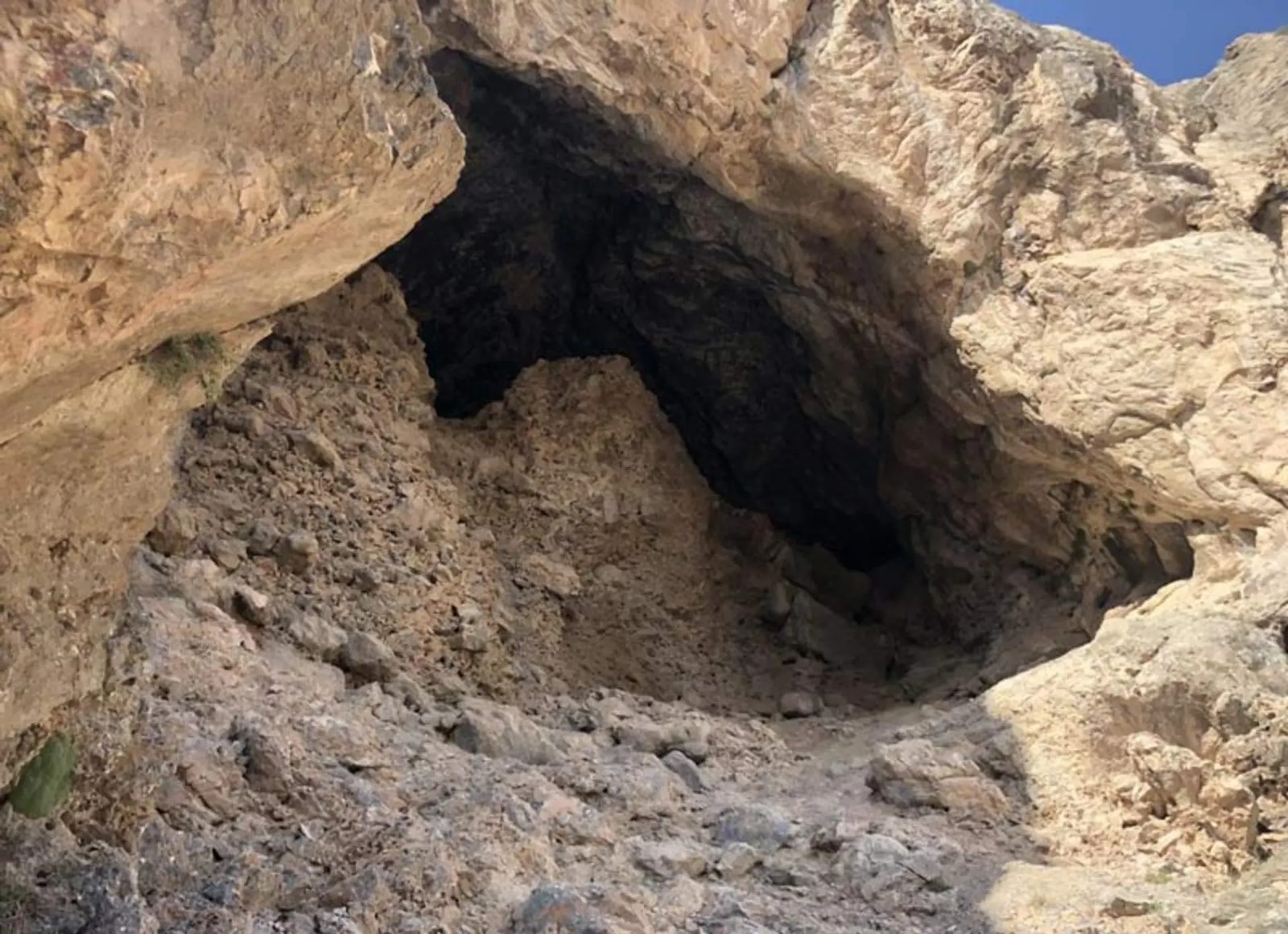 At the entrance, a slope of broken rock fills the mouth beneath sun-bleached stone