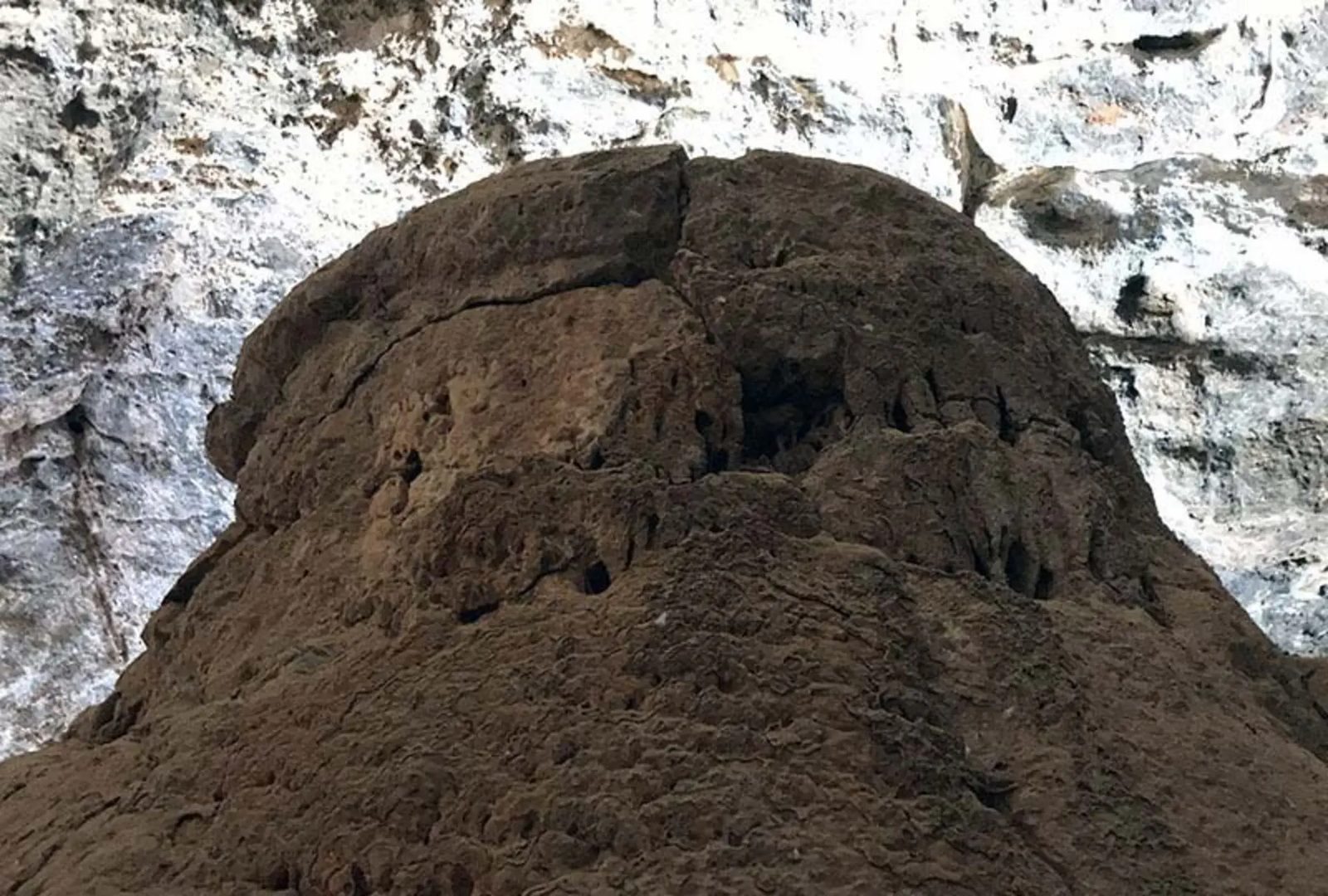 A rounded mass of hardened sediment rises against the pale, weathered rock wall
