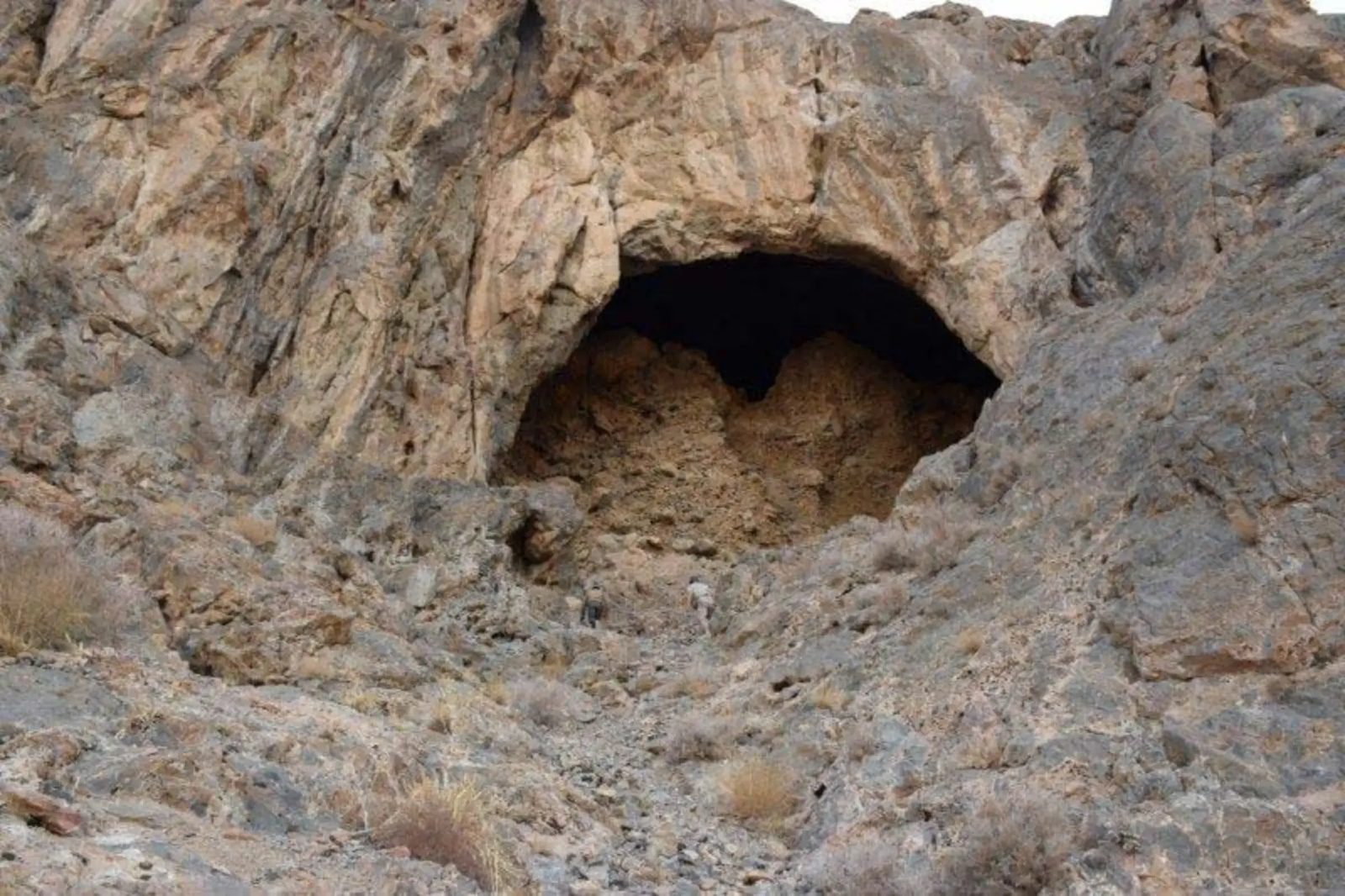 The trail up to the cave mouth, two climbers on the loose rock beneath the pale arch