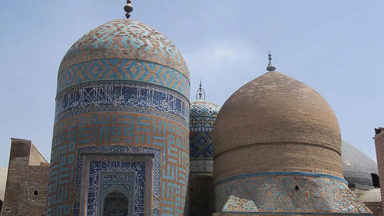 Tomb towers of the Sheikh Safi al-Din shrine complex in Ardabil, one sheathed in turquoise and saffron glazed tile with a band of Kufic inscription, the other in bare brick
