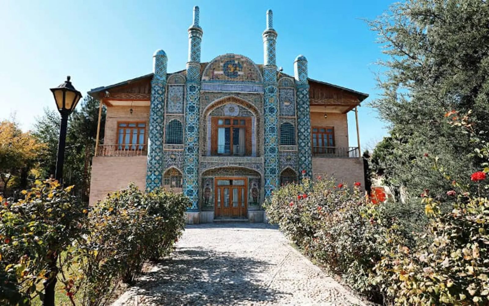 Tiled Qajar facade of the Ayineh Khaneh mansion with a rose bed along the approach path