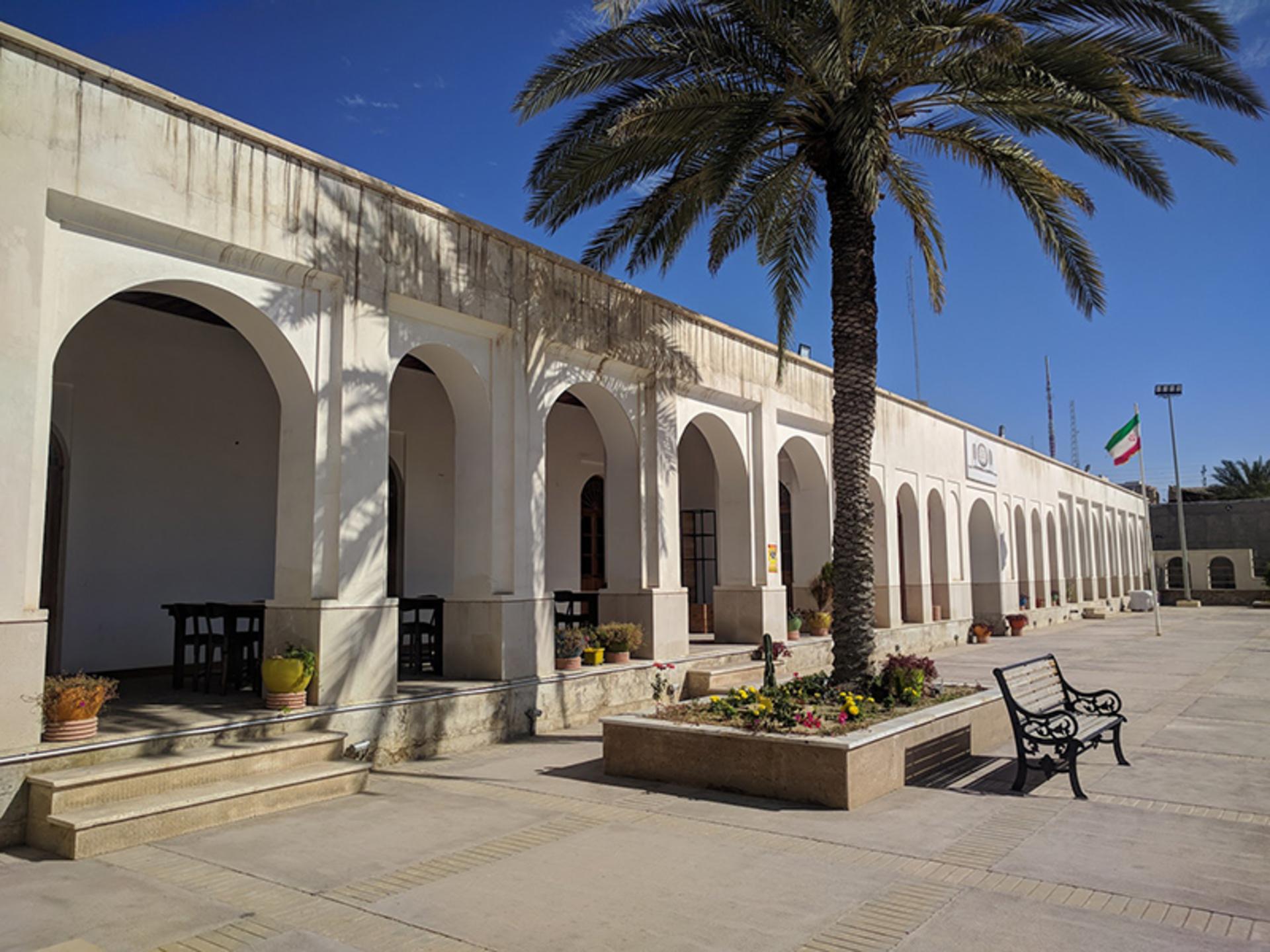 Whitewashed arcade with rounded arches and a palm tree in the sunlit courtyard of a historic Bushehr school