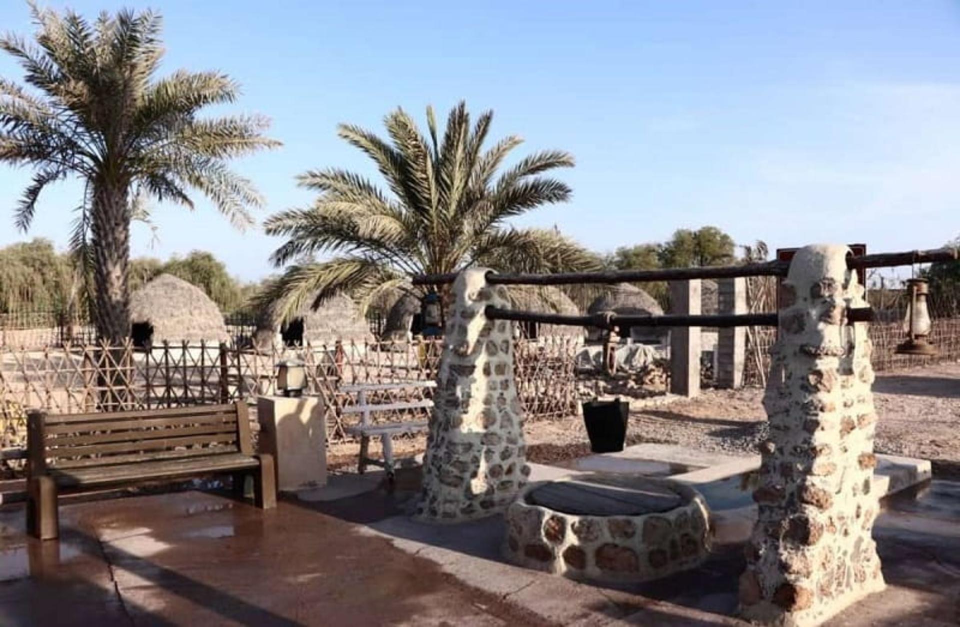 Stone well monument and thatched dome huts among date palms in Baghku, old Kish