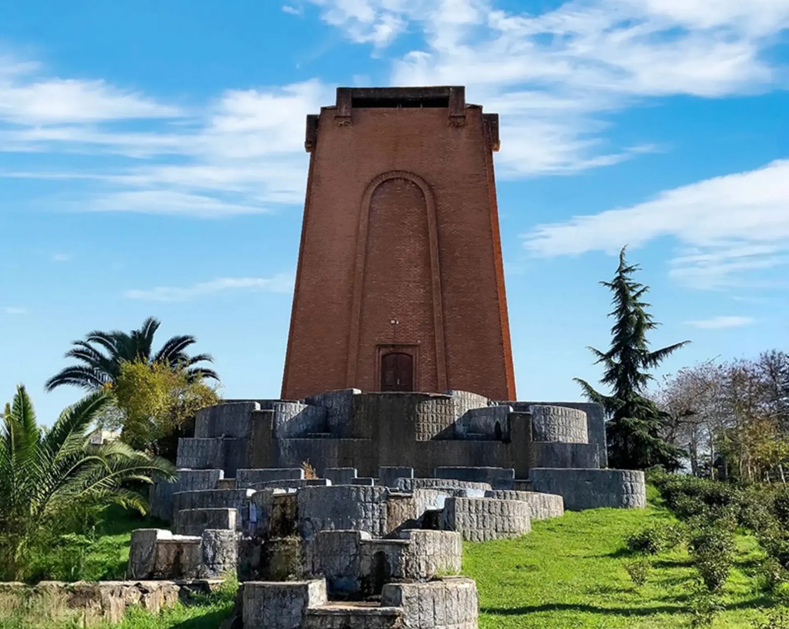 Tapering red-brick tower of the Kashef ol-Soltaneh tomb above a stepped rock cascade