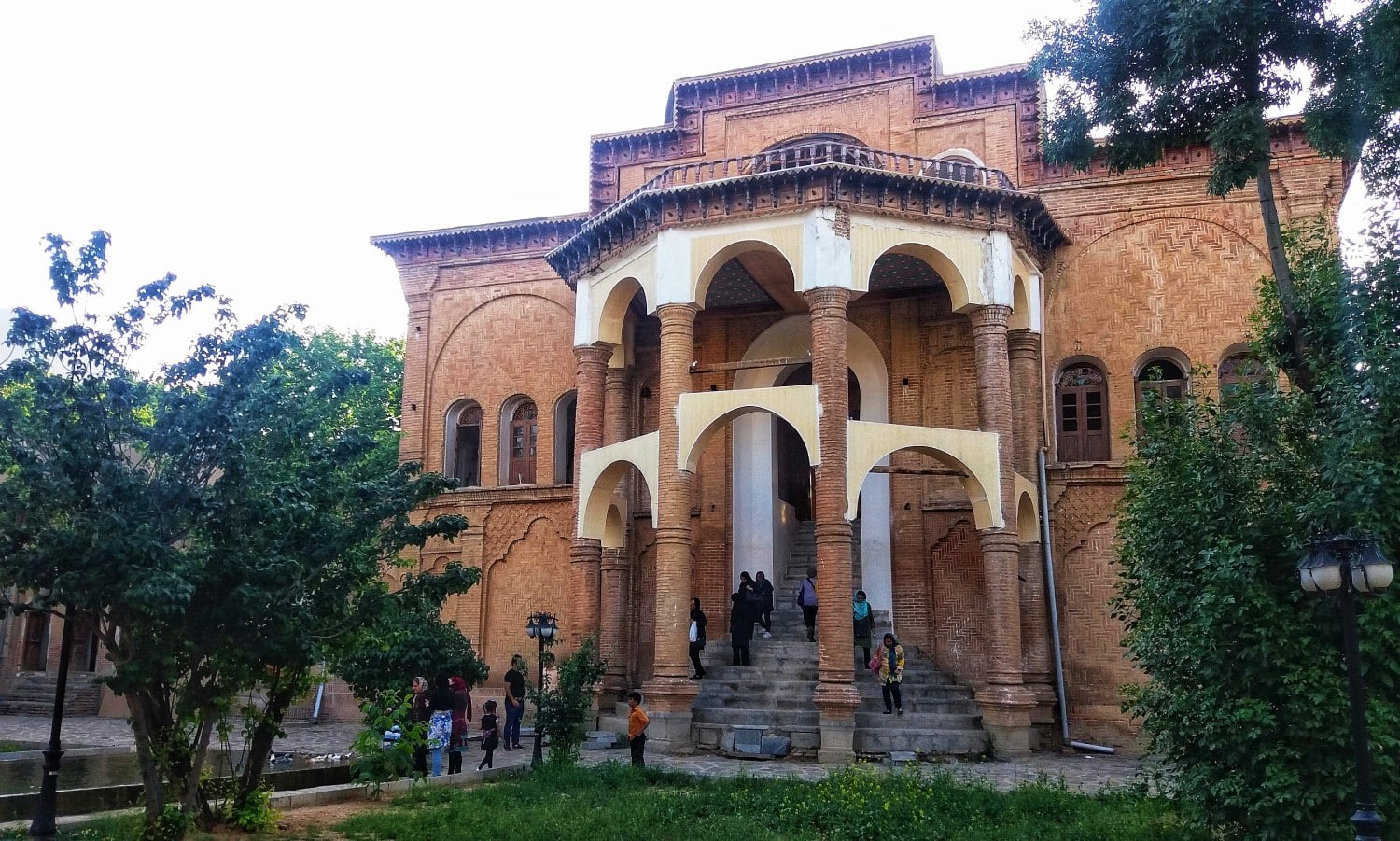 Khosroabad Mansion surrounded by a large garden with tall trees and a central pool